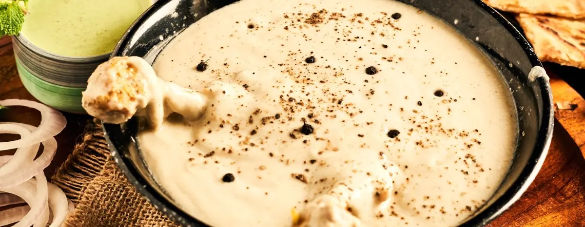 A bowl of white pepper sauce with chicken pieces and dark pepper specks.
