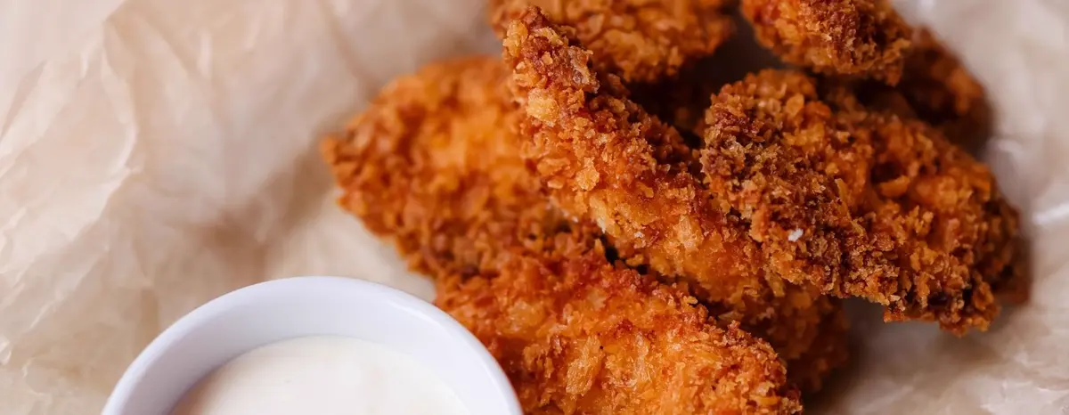 Breaded chicken tenders beside a small white cup of dipping sauce.