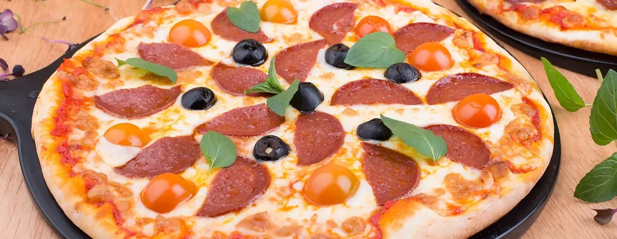 Pepperoni pizza with tomatoes, olives and basil leaves.